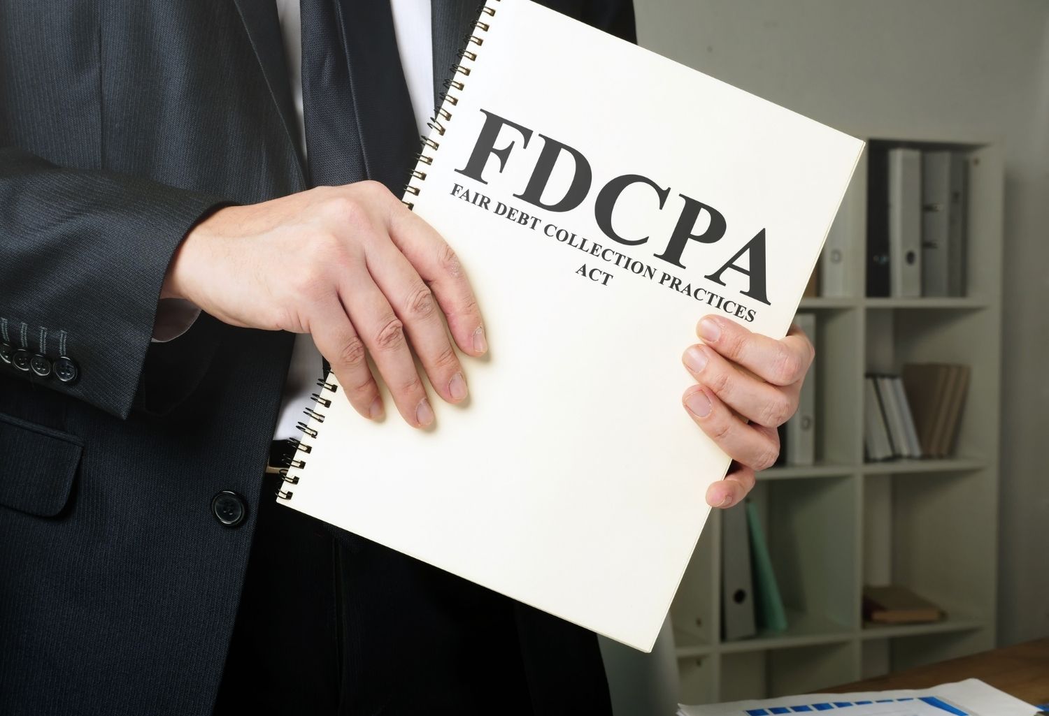 Suited man holding a notebook labeled FDCPA, Fair Debt Collection Practices Act. Representing Ethical Debt Collection.