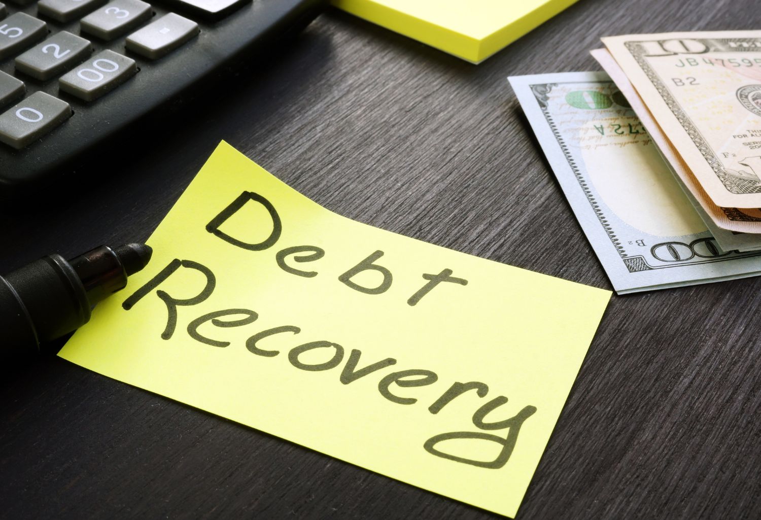 Sticky note laid out on a black wood desk with the words debt recovery written in black marker.